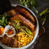 Overhead close-up of Use What You Have Ramen in a rustic speckled ceramic bowl filled with rich amber miso-tonkotsu broth