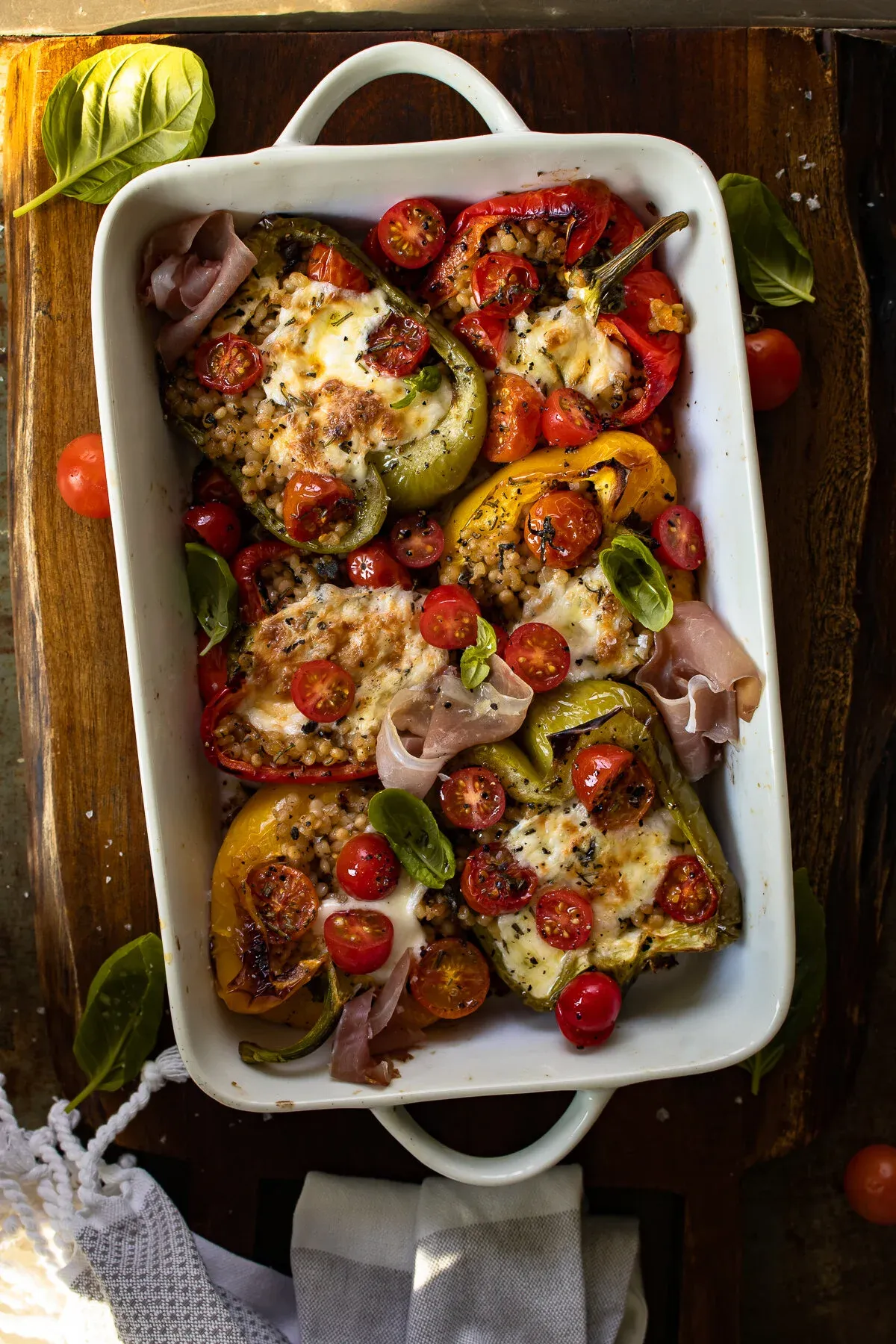Overhead shot of a white rectangular handled baking dish on a dark wood board filled with Couscous Stuffed Roasted Bell Peppers with Fresh Mozzarella