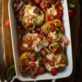 Overhead shot of a white rectangular handled baking dish on a dark wood board filled with Couscous Stuffed Roasted Bell Peppers with Fresh Mozzarella