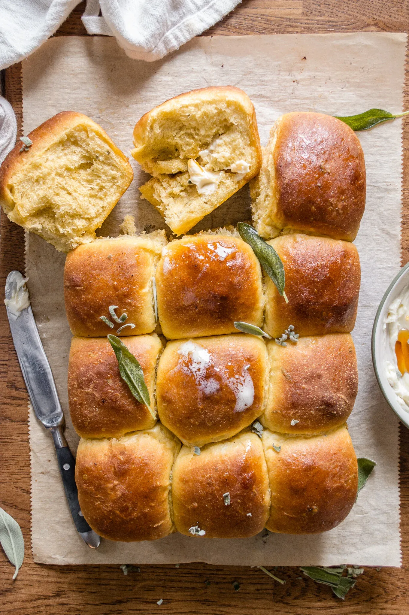 Overhead view of pumpkin and fried sage honey bread rolls arranged in a 3x4 grid on parchment paper on a wooden board