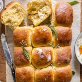 Overhead view of pumpkin and fried sage honey bread rolls arranged in a 3x4 grid on parchment paper on a wooden board