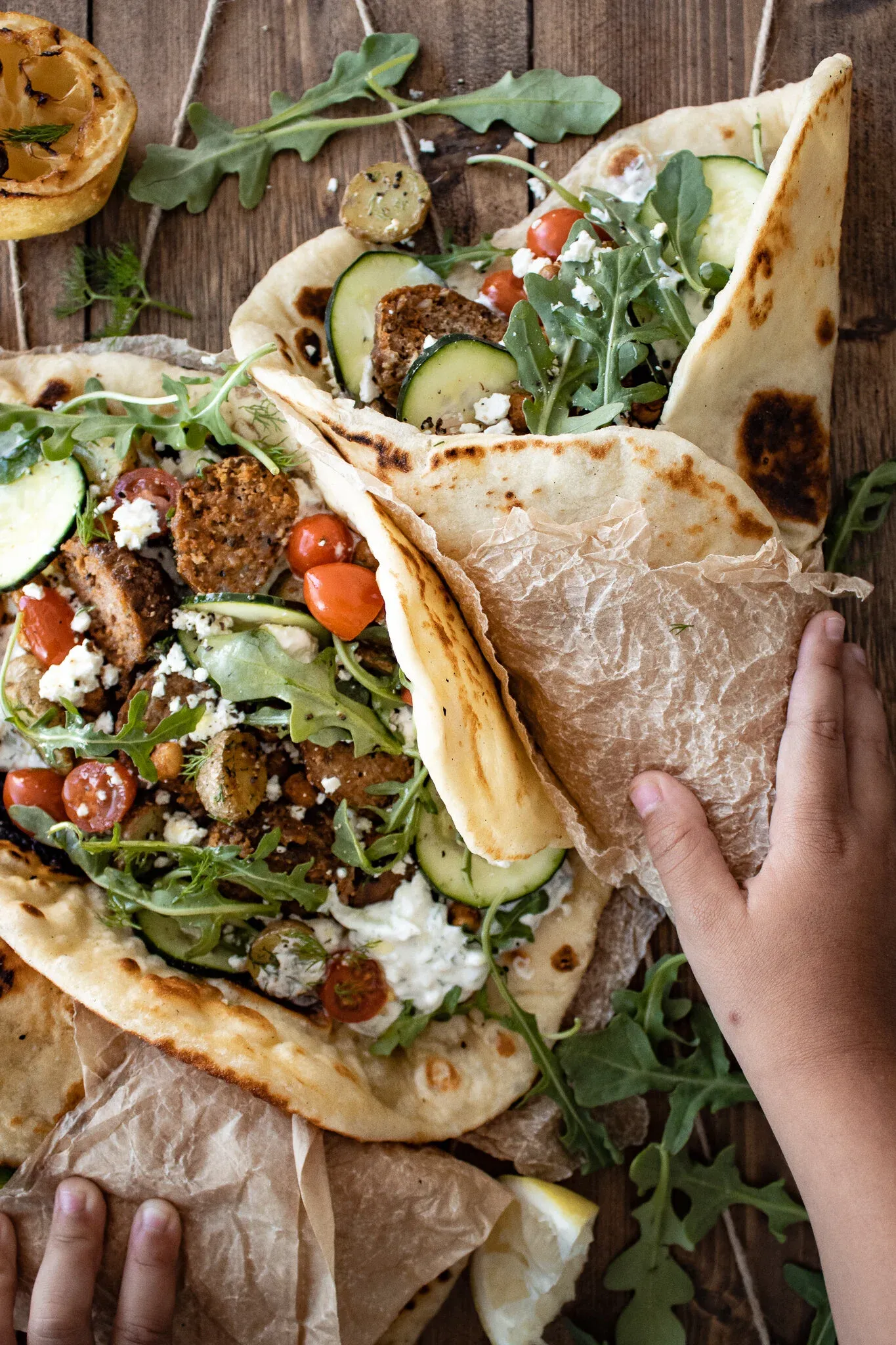 Two open-faced lamb wraps on charred flatbread piled with spiced ground lamb pieces, fresh arugula, halved cherry tomatoes
