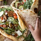Two open-faced lamb wraps on charred flatbread piled with spiced ground lamb pieces, fresh arugula, halved cherry tomatoes