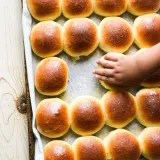 Rows of honey bread rolls with deep golden-brown glossy domed tops packed tightly in a parchment-lined baking pan