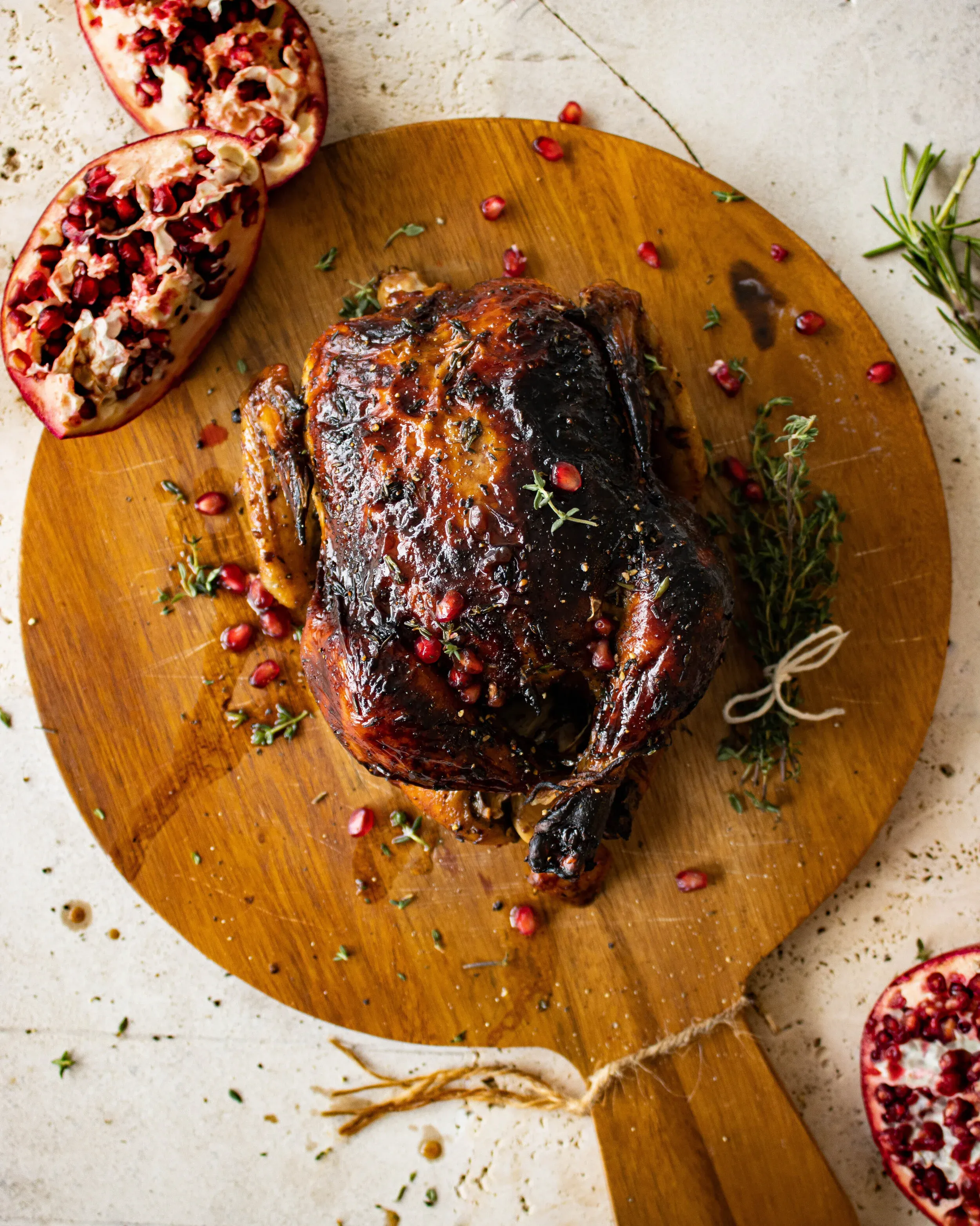 Whole Balsamic and Pomegranate Roasted Chicken with deeply lacquered mahogany-dark glazed skin resting on a round wooden paddle board
