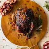 Whole Balsamic and Pomegranate Roasted Chicken with deeply lacquered mahogany-dark glazed skin resting on a round wooden paddle board