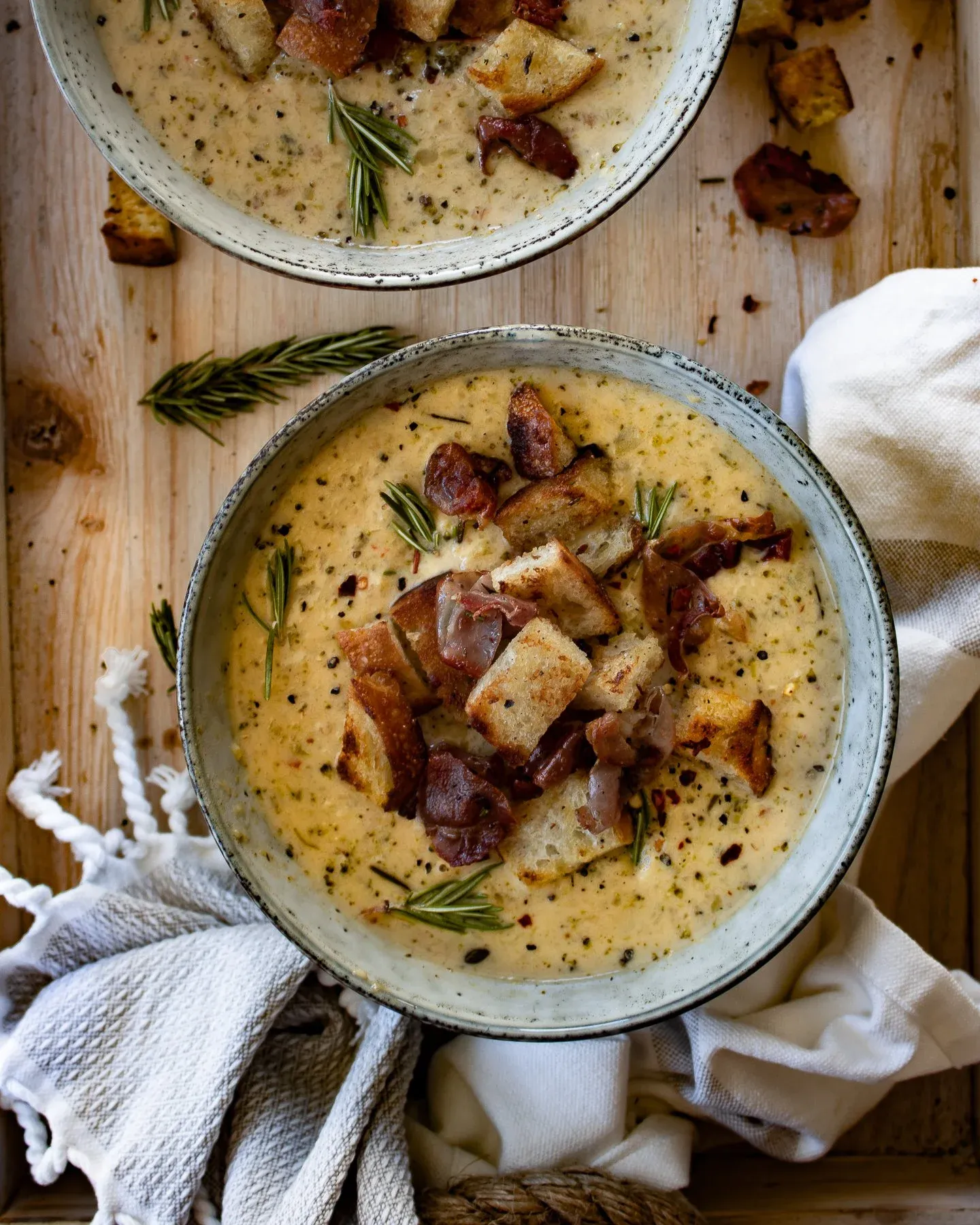 Two rustic gray speckled ceramic bowls of One Pot Broccoli and Zucchini Cheddar Soup on a light wood board