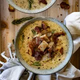 Two rustic gray speckled ceramic bowls of One Pot Broccoli and Zucchini Cheddar Soup on a light wood board