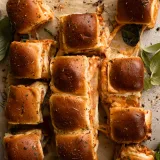 Overhead flat-lay of prosciutto and cheese pull-apart sliders on parchment paper on a light gray surface