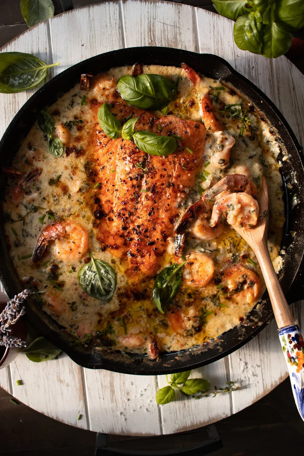 Overhead view of a black cast iron skillet on a white painted wood surface holding Saucy Salmon and Shrimp in Coconut Milk with Spinach