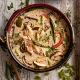 Tom Kha Gai (Thai Coconut Chicken Soup) in a large shallow copper pan with dark red rim