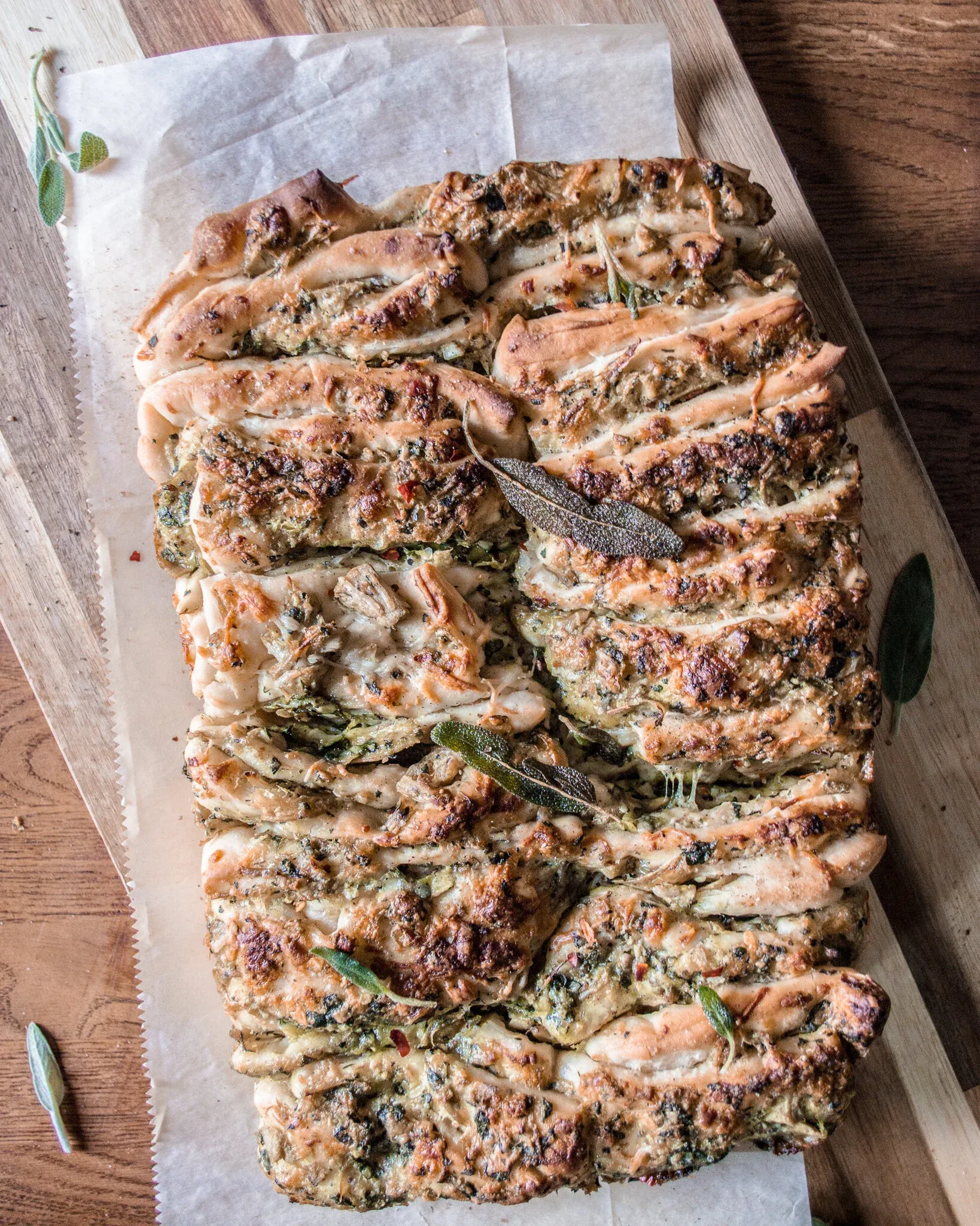 Overhead view of a whole cheesy spinach and artichoke pull-apart bread loaf on parchment paper on a wooden cutting board