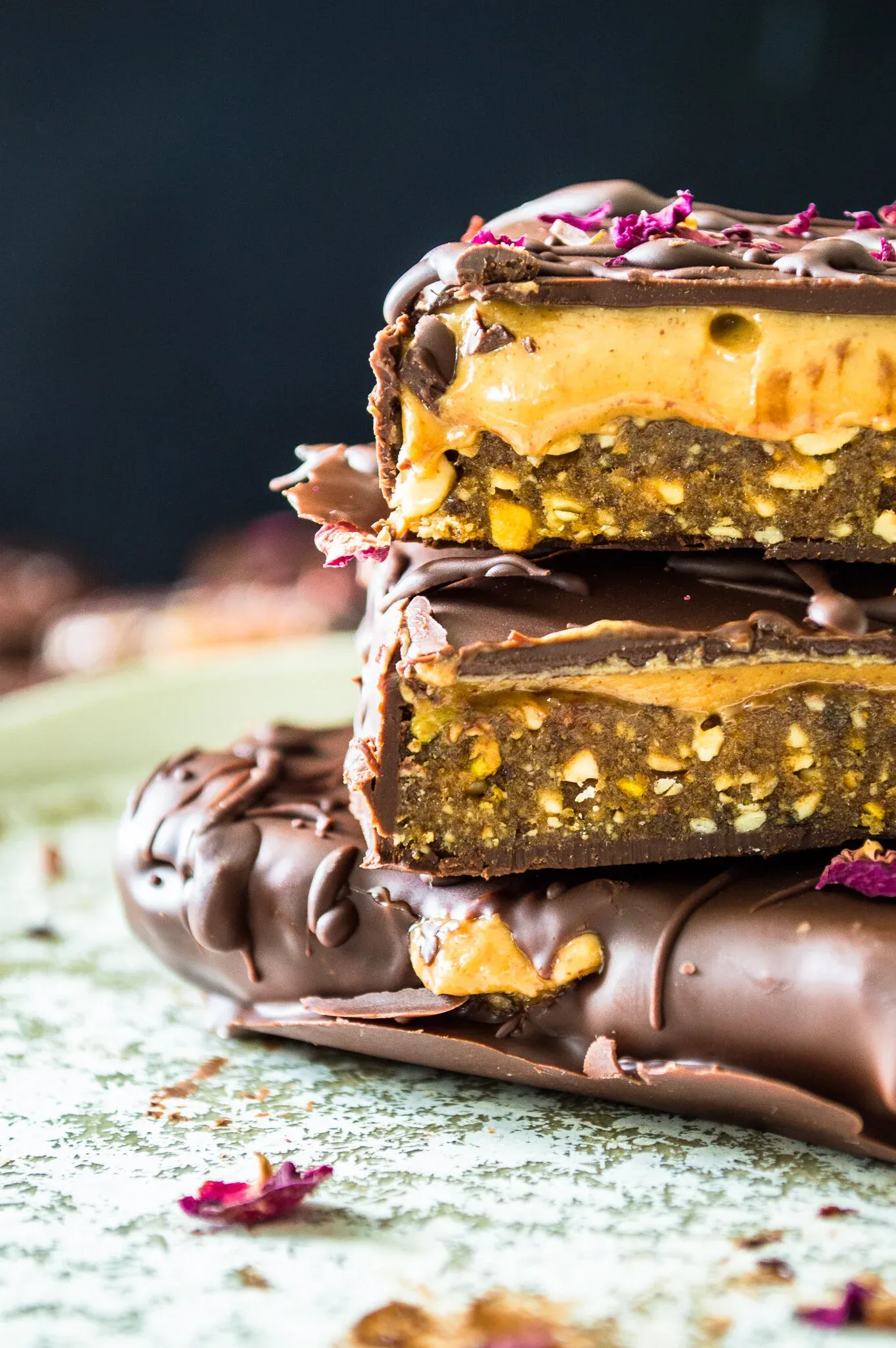 Side-angle close-up of three stacked No Bake Dark Chocolate Nut Butter Bars on a green mottled surface