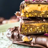 Side-angle close-up of three stacked No Bake Dark Chocolate Nut Butter Bars on a green mottled surface