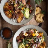 Overhead view of two gray speckled bowls of Sheet Pan Pineapple Chicken Bowls on a wooden tray