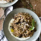 Overhead shot of a grey speckled stoneware bowl of Farro Risotto with Mushrooms and Whipped Ricotta in the foreground