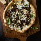 Mushroom and Goat Cheese Pizza on a wooden pizza peel, the puffy charred artisan crust topped with creamy goat cheese