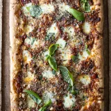 Overhead view of a whole rectangular Sicilian-inspired sheet pan pizza on a rustic wooden board