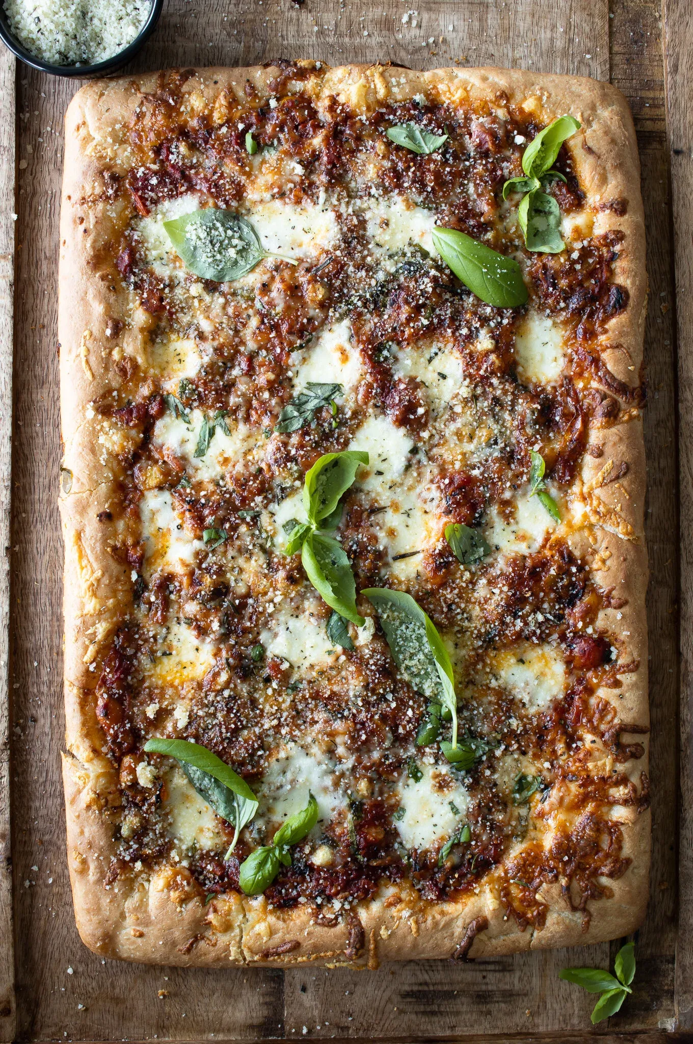 Overhead view of a whole rectangular Sicilian-inspired sheet pan pizza on a rustic wooden board