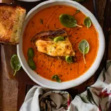 One Pot Roasted Tomato and Herb Soup with Halloumi Toast in a white ceramic bowl, overhead view on a dark wooden board