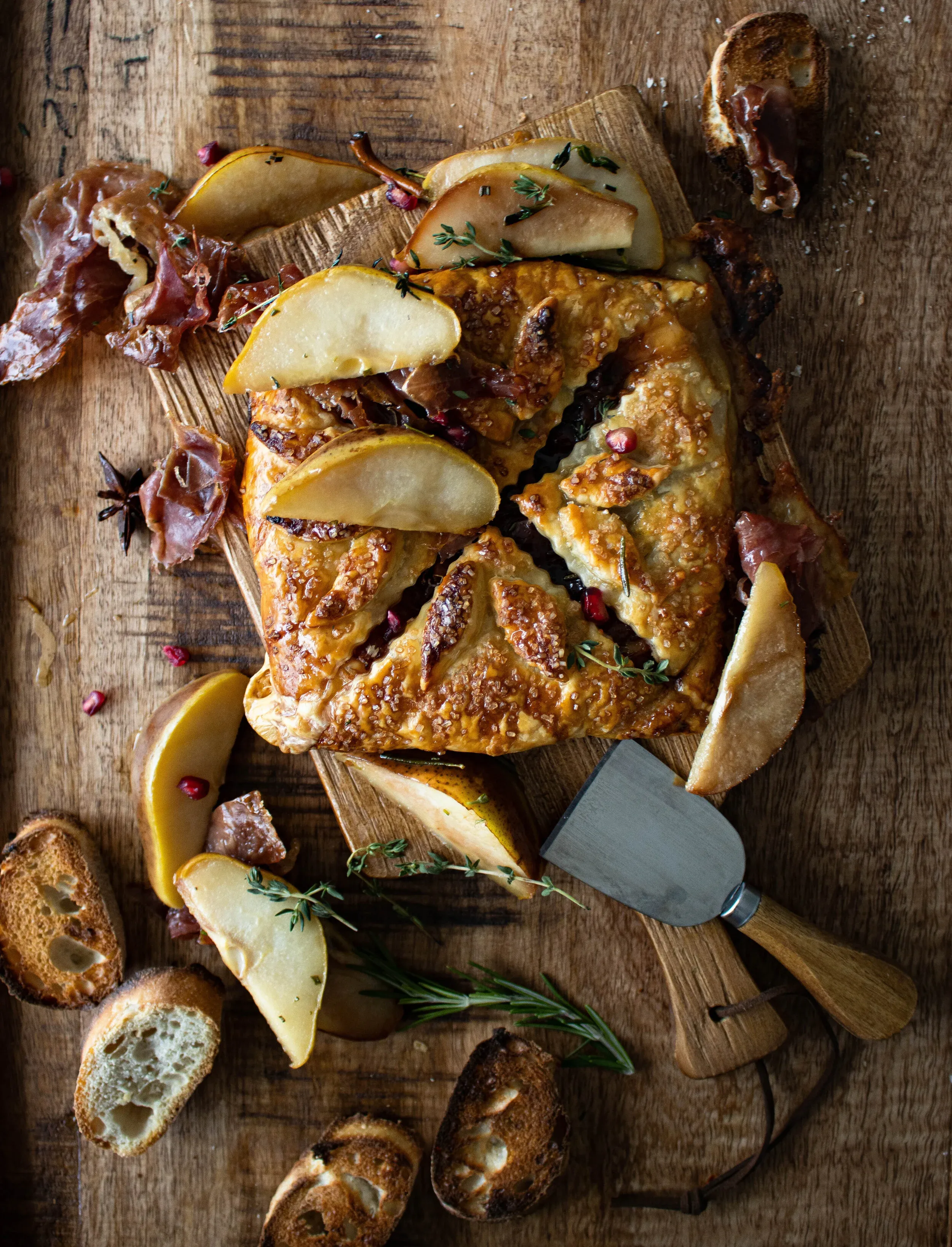 Overhead shot of Wrapped Brie and Prosciutto with Herbed Honey Peaches on a rustic wood cutting board
