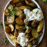 Overhead view of Roasted Herby Potatoes with Burrata in a large white oval bowl on a rustic wooden surface
