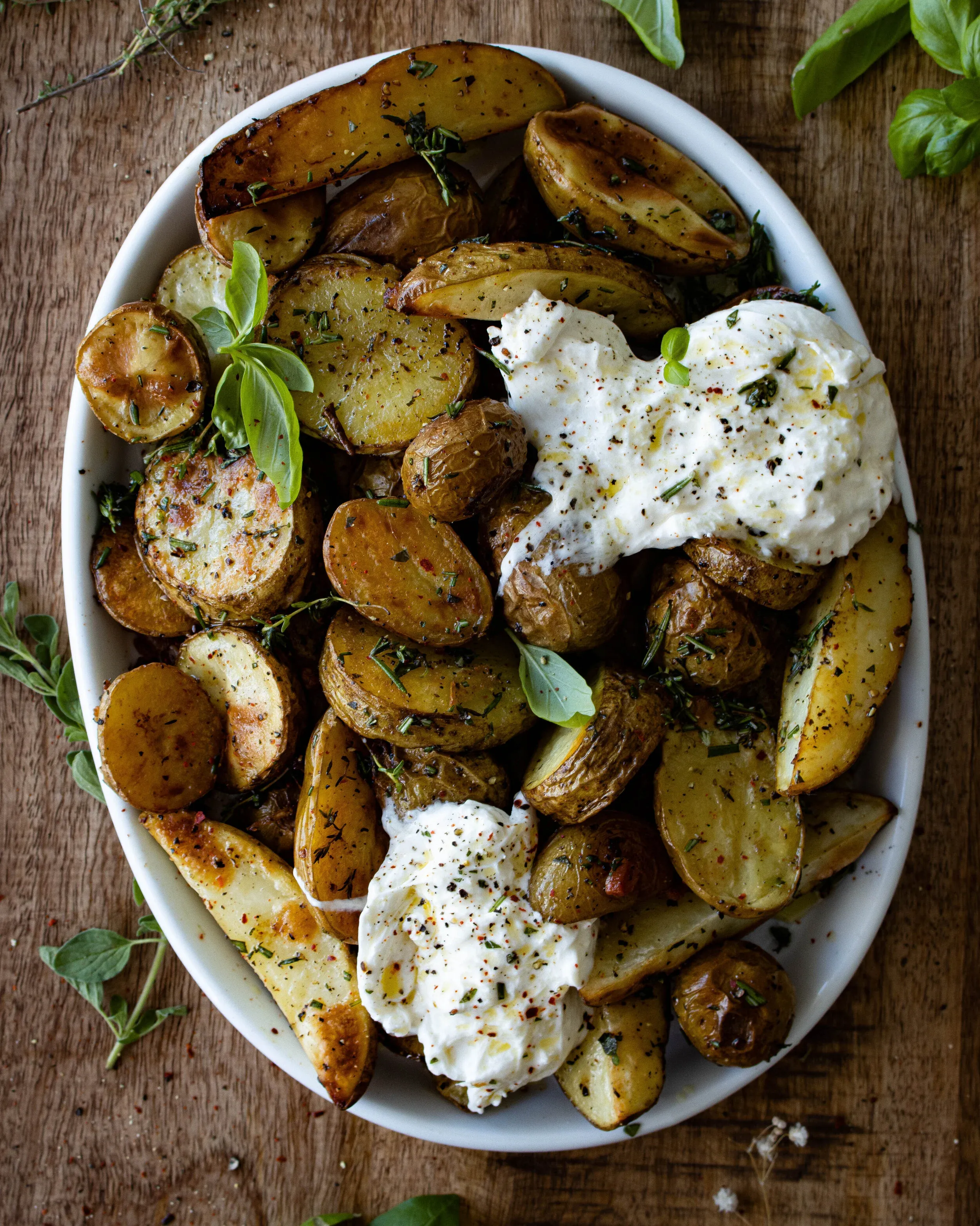 Overhead view of Roasted Herby Potatoes with Burrata in a large white oval bowl on a rustic wooden surface