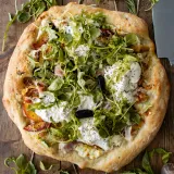 Overhead close-up of a whole Burrata and Rosemary Peach Pizza on a dark wood board