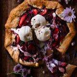 Overhead dark-moody shot of a rustic poached peach galette on a dark wood board