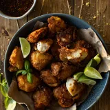 Batter Fried Chicken pieces piled in a dark blue ceramic bowl lined with parchment paper