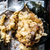 Close angled overhead shot of a dark baking sheet with a deeply roasted dark green acorn squash half overflowing with Crab Mac and Cheese