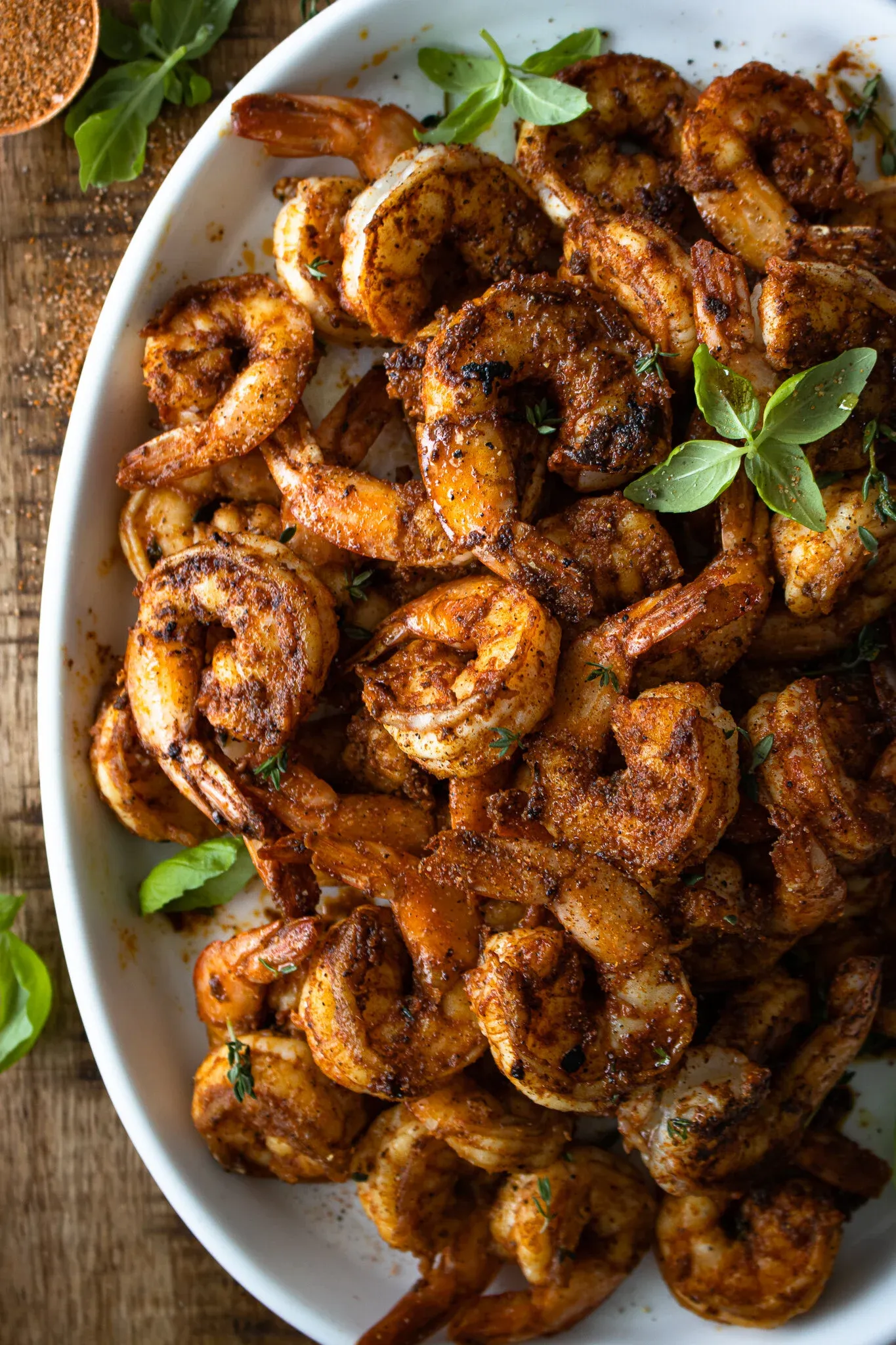 Overhead close-up of a large white oval platter piled high with Cajun-seared shrimp for Cajun Shrimp with Kale Polenta