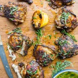 Overhead flat-lay of eight cast iron grilled chicken thighs on a large wooden cutting board