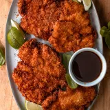 Overhead view of two large mojo chicken katsu cutlets on a grey oval ceramic platter on a round wooden cutting board