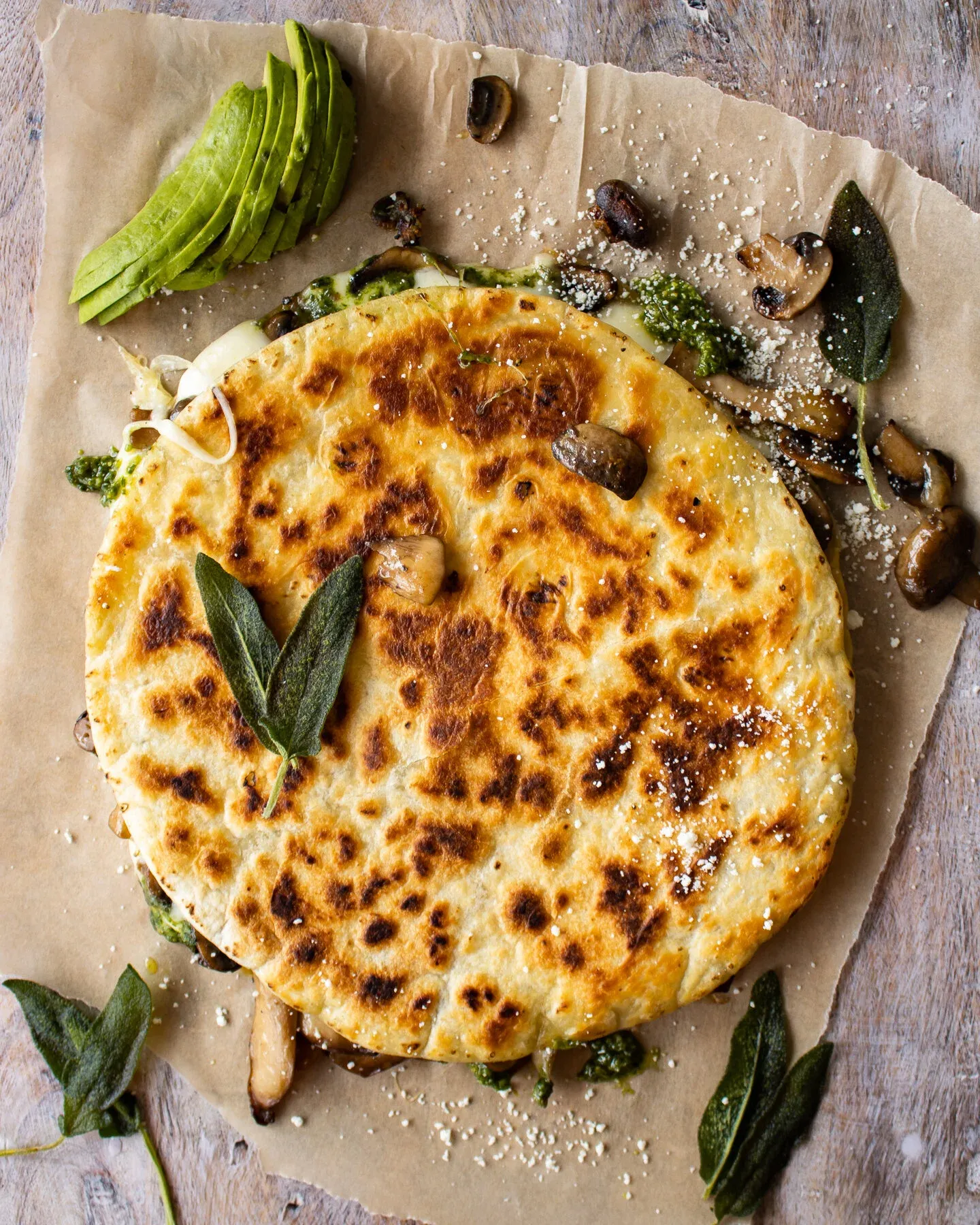 Overhead view of a whole uncut Wild Mushroom and Pesto Quesadilla on brown parchment paper