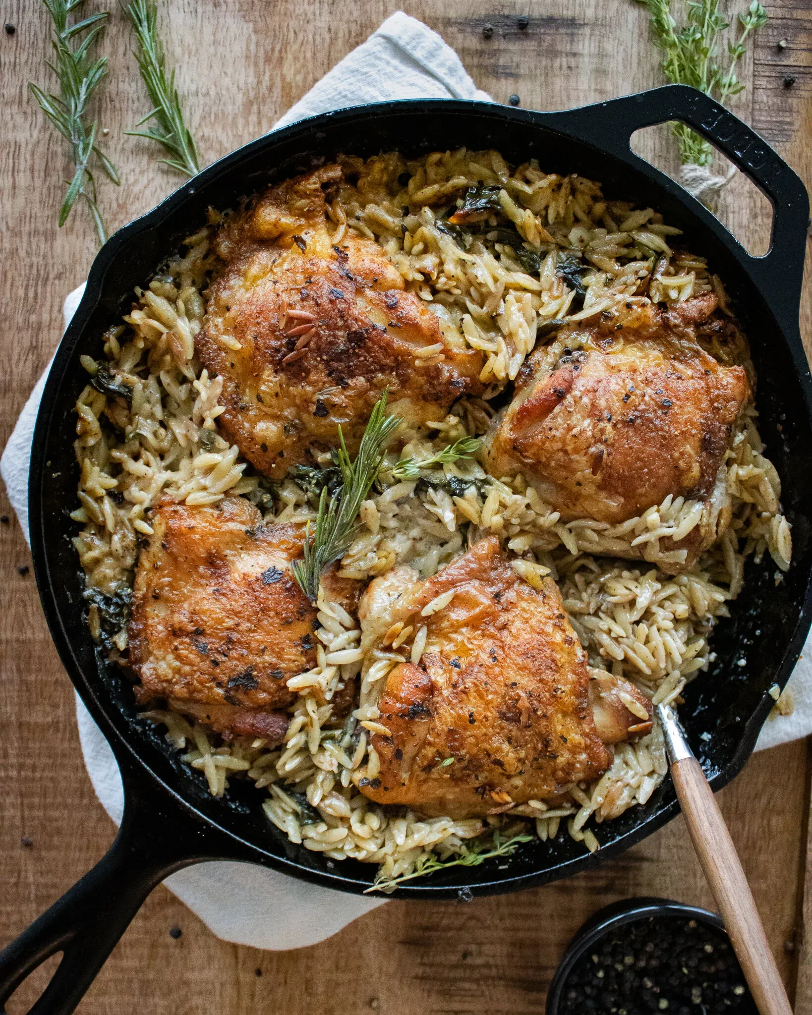 One Skillet Spinach Chicken and Orzo in a black cast iron pan set on a wooden surface with a white linen underneath