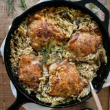 One Skillet Spinach Chicken and Orzo in a black cast iron pan set on a wooden surface with a white linen underneath