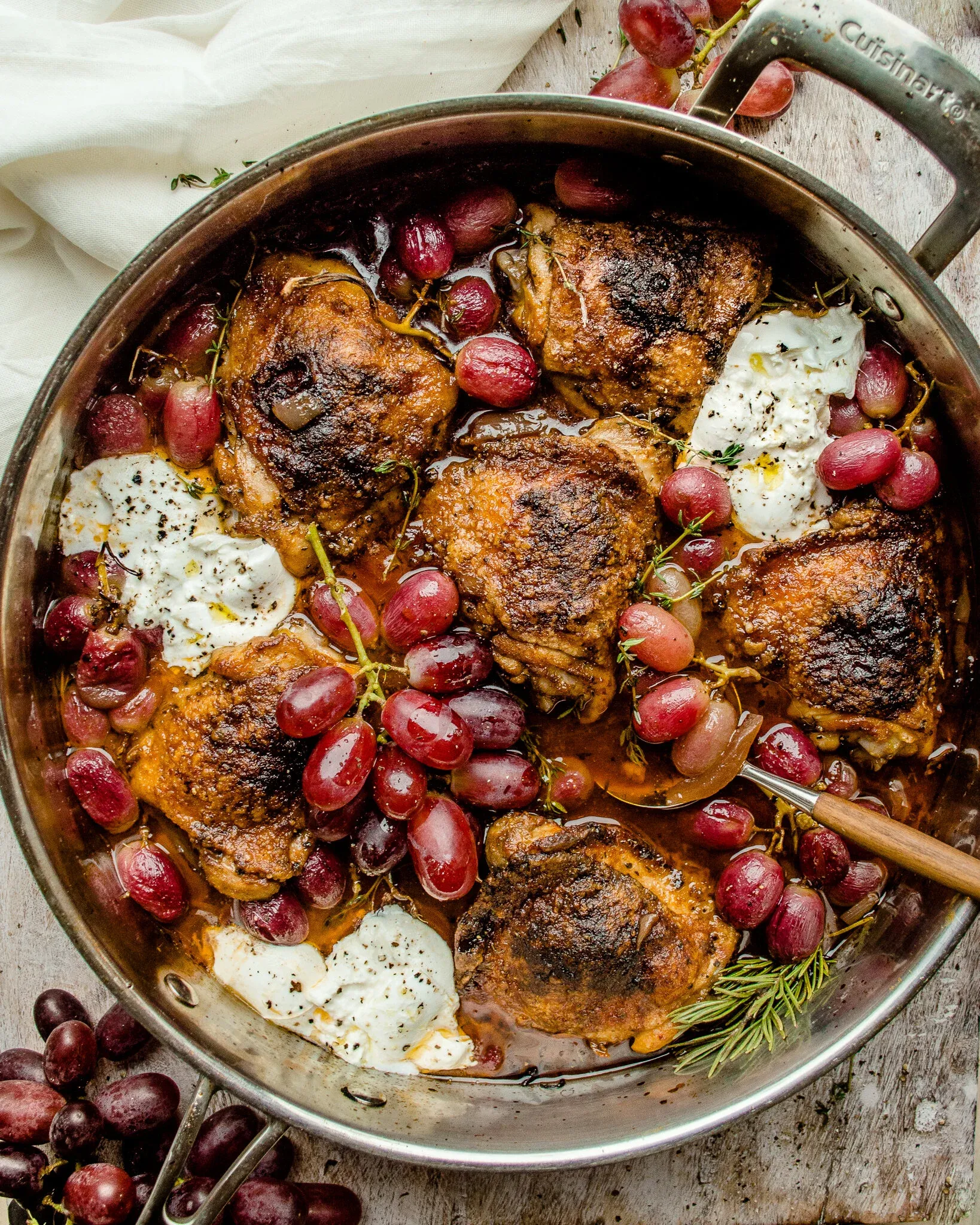 Overhead view of red wine and balsamic braised chicken thighs with grapes and burrata in a large stainless steel skillet