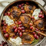 Overhead view of red wine and balsamic braised chicken thighs with grapes and burrata in a large stainless steel skillet