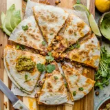 Crispy Chickpea and Cauliflower Quesadilla sliced into eight wedges and arranged overhead on a striped wooden cutting board