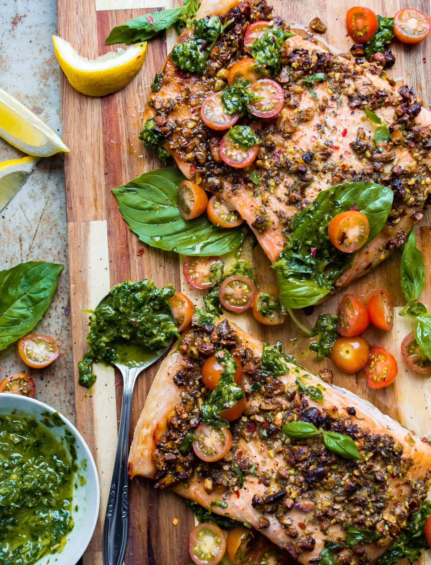 Angled overhead shot of two baked pistachio-crusted salmon fillets on a wooden cutting board