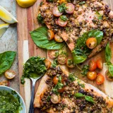Angled overhead shot of two baked pistachio-crusted salmon fillets on a wooden cutting board