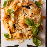 Spinach and Feta Phyllo Pie as a rustic round galette on a white ceramic paddle board, overhead view on a dark background