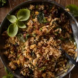 Overhead close-up of pork belly, mushroom and crispy basil fried rice filling a large stainless steel sauté pan