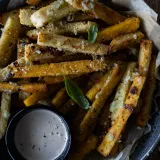 Overhead close-up of parmesan and herb polenta fries piled in a dark navy speckled ceramic bowl lined with parchment paper