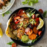 Overhead view of a black ceramic bowl with a serving of chicken and vegetable skewers with roasted sweet potatoes