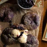 Multiple Ube and Blueberry Mini Pies on parchment paper on a dark wooden board, angled overhead view