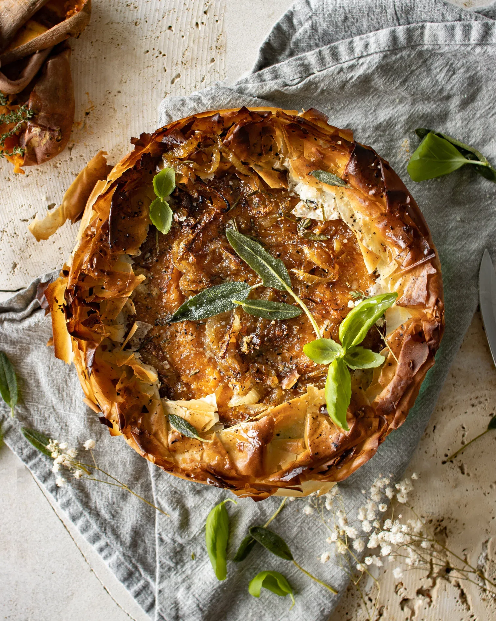 Overhead view of a whole sweet potato, spinach and caramelized onion phyllo pie with a deeply golden