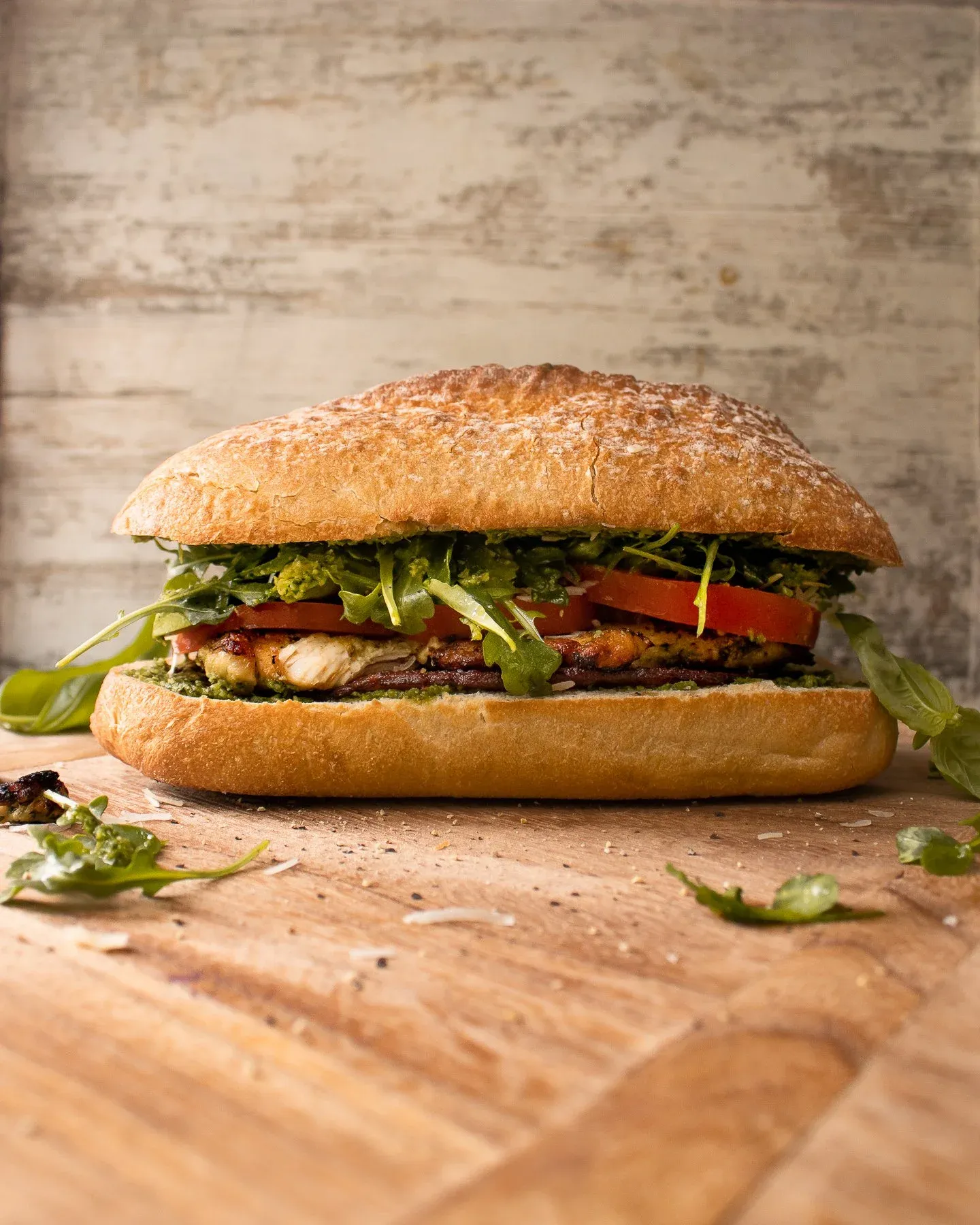 Pesto Chicken BLT Sandwich on a crusty golden ciabatta roll standing upright on a light wood cutting board