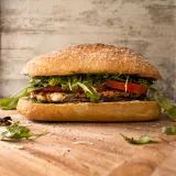 Pesto Chicken BLT Sandwich on a crusty golden ciabatta roll standing upright on a light wood cutting board